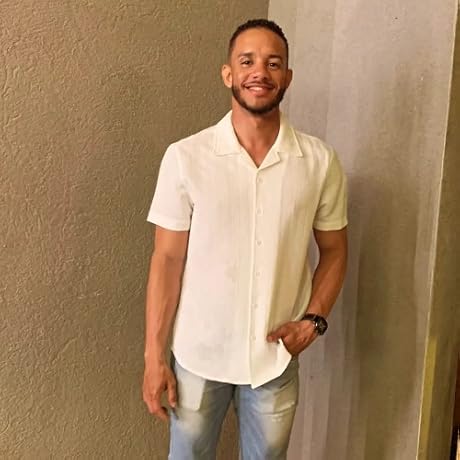 Man wearing a light-colored shirt and jeans against a plain wall