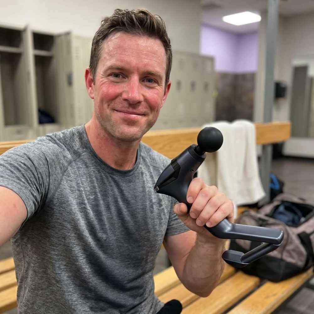 Man holding a massage gun in a locker room setting